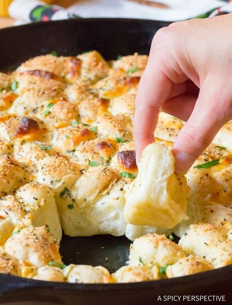 a person dipping some food into a skillet with cheese and herbs on the side