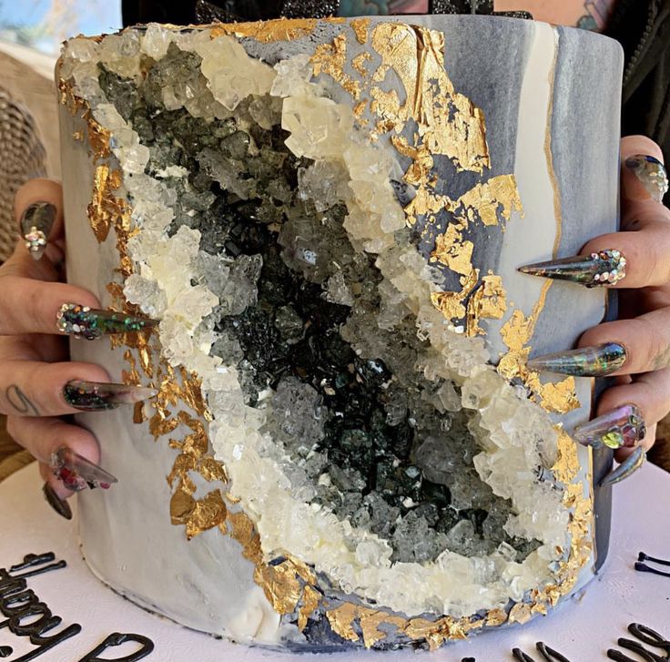 a woman holding a large piece of art with gold and silver paint on it's face