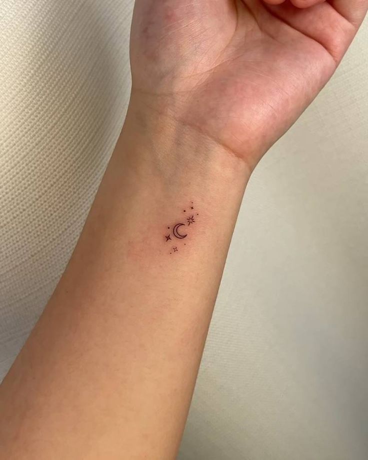 a woman's wrist with a small star and moon tattoo on the left arm