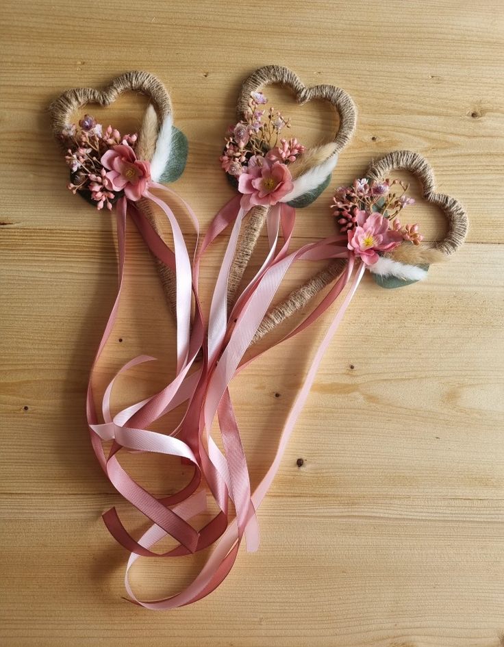 three heart shaped flowers with pink ribbons on a wooden table next to eachother