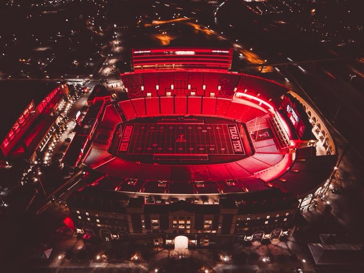 an aerial view of a stadium at night with bright red lights on the sidelines