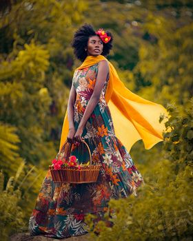 a woman standing in the woods holding a basket and wearing a yellow scarf over her head