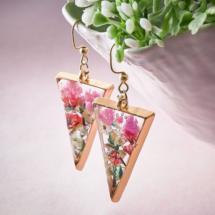 a pair of triangle shaped earrings with flowers on them sitting next to a potted plant