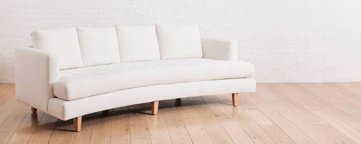 a white couch sitting on top of a hard wood floor next to a brick wall