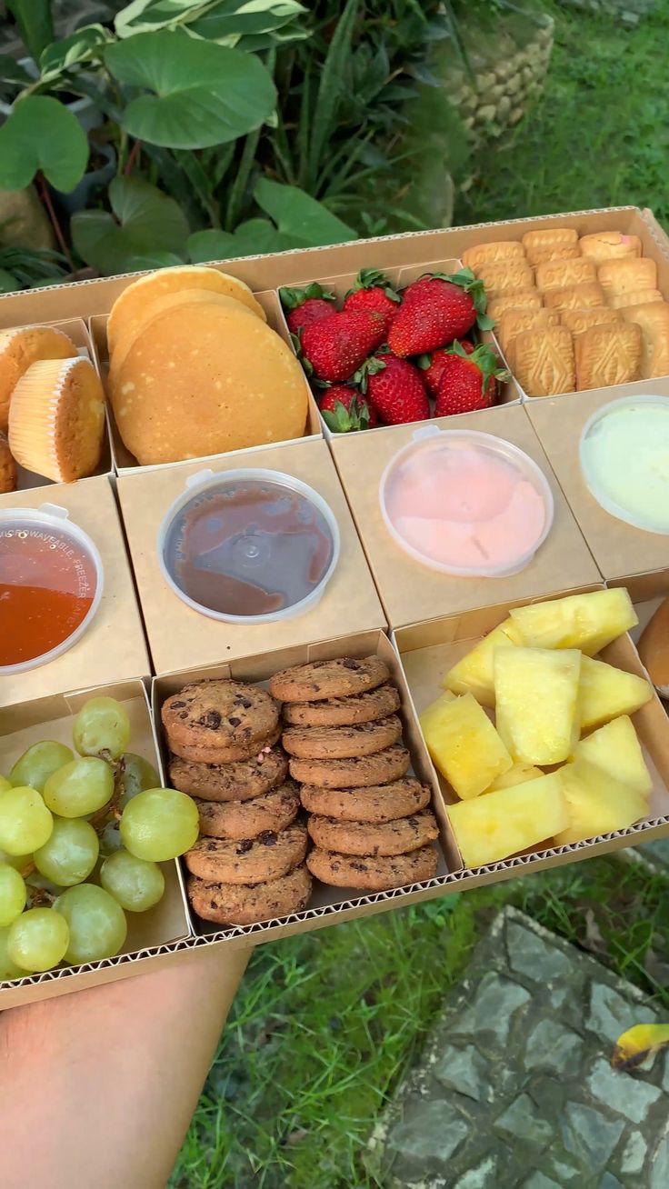 an open box filled with lots of different types of food next to fruit and bread