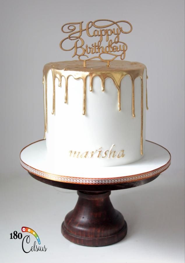 a white and gold birthday cake with the words happy birthday written on it, sitting on top of a wooden stand