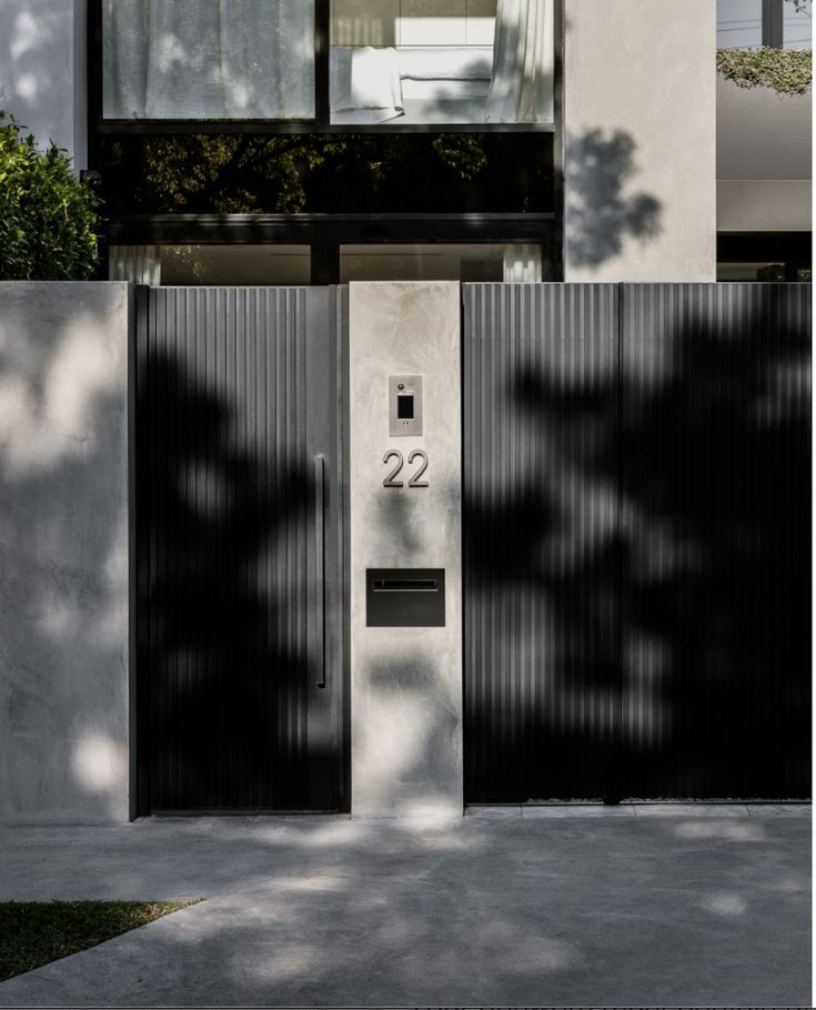 two black doors are open in front of a white building with trees on the other side