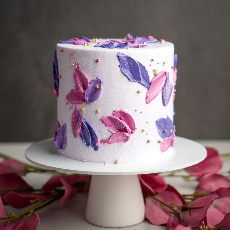 a white cake with purple and pink frosting on top of a table next to flowers