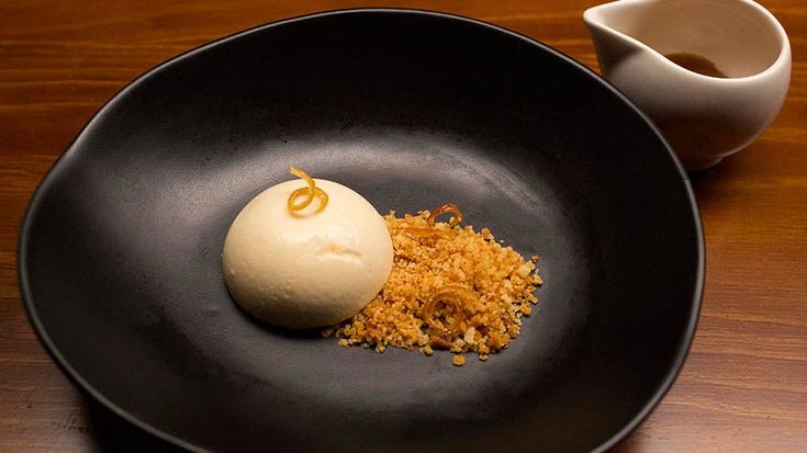 a black plate topped with an ice cream ball and crumbs next to a cup