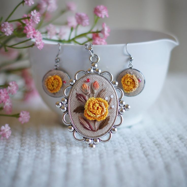 a close up of a necklace and earrings on a table with flowers in the background