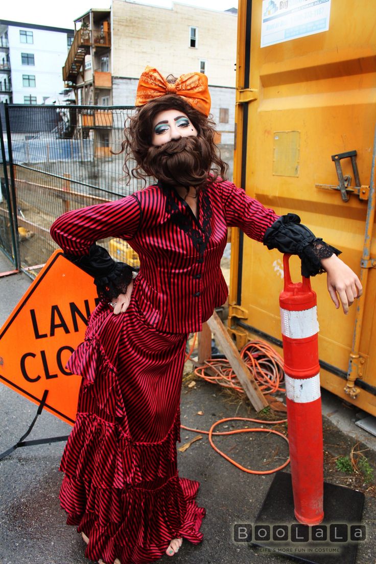 a woman in a red and black dress standing next to a fire hydrant wearing a fake beard