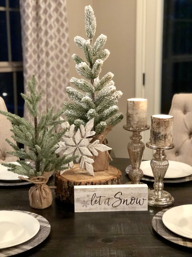 a dining room table set for christmas with white plates and silver candlesticks on it