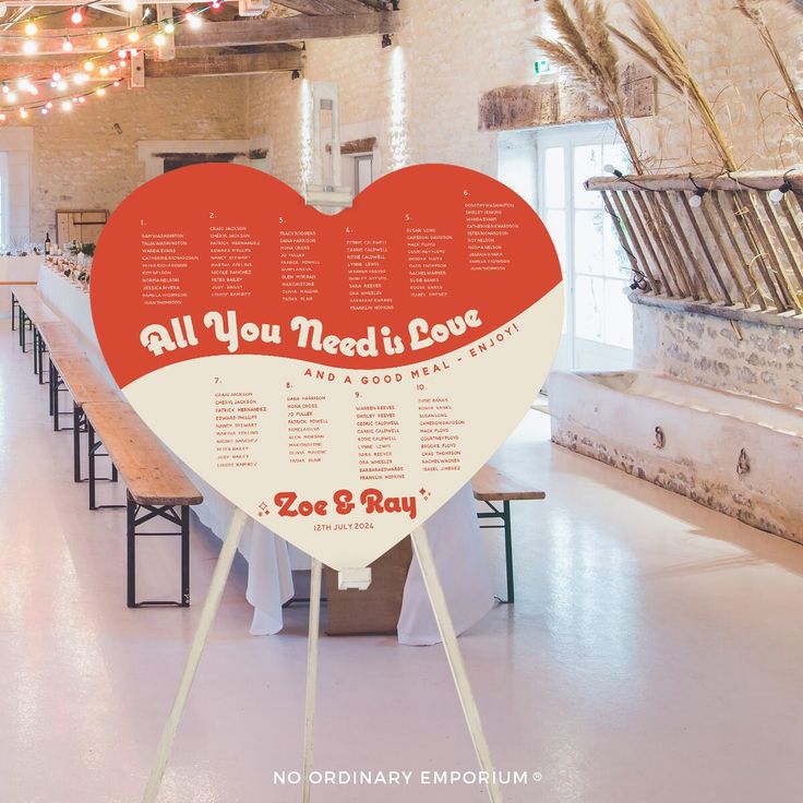 a large red heart shaped sign sitting in the middle of a room with tables and benches