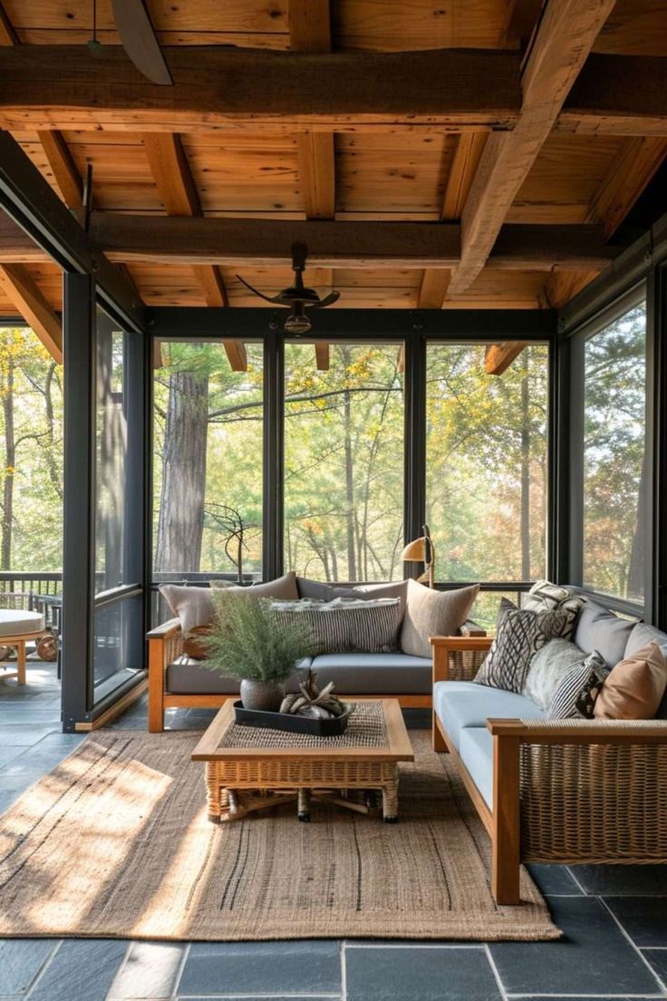 a living room with couches and tables on the outside patio, looking out onto the woods