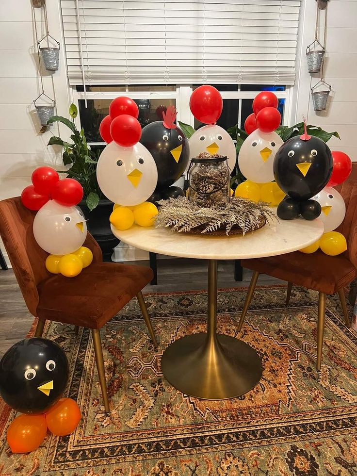 a table topped with balloons and penguins sitting on chairs next to each other in front of a window