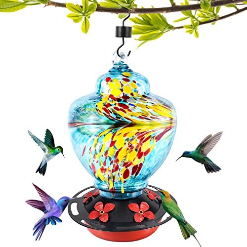 colorful glass bird feeder hanging from a tree branch with two hummingbirds flying around it