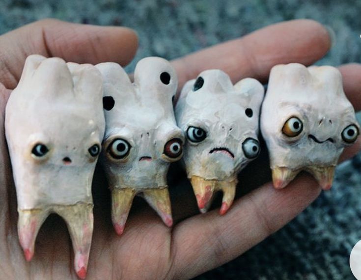 a hand holding five fake teeth with eyes on them