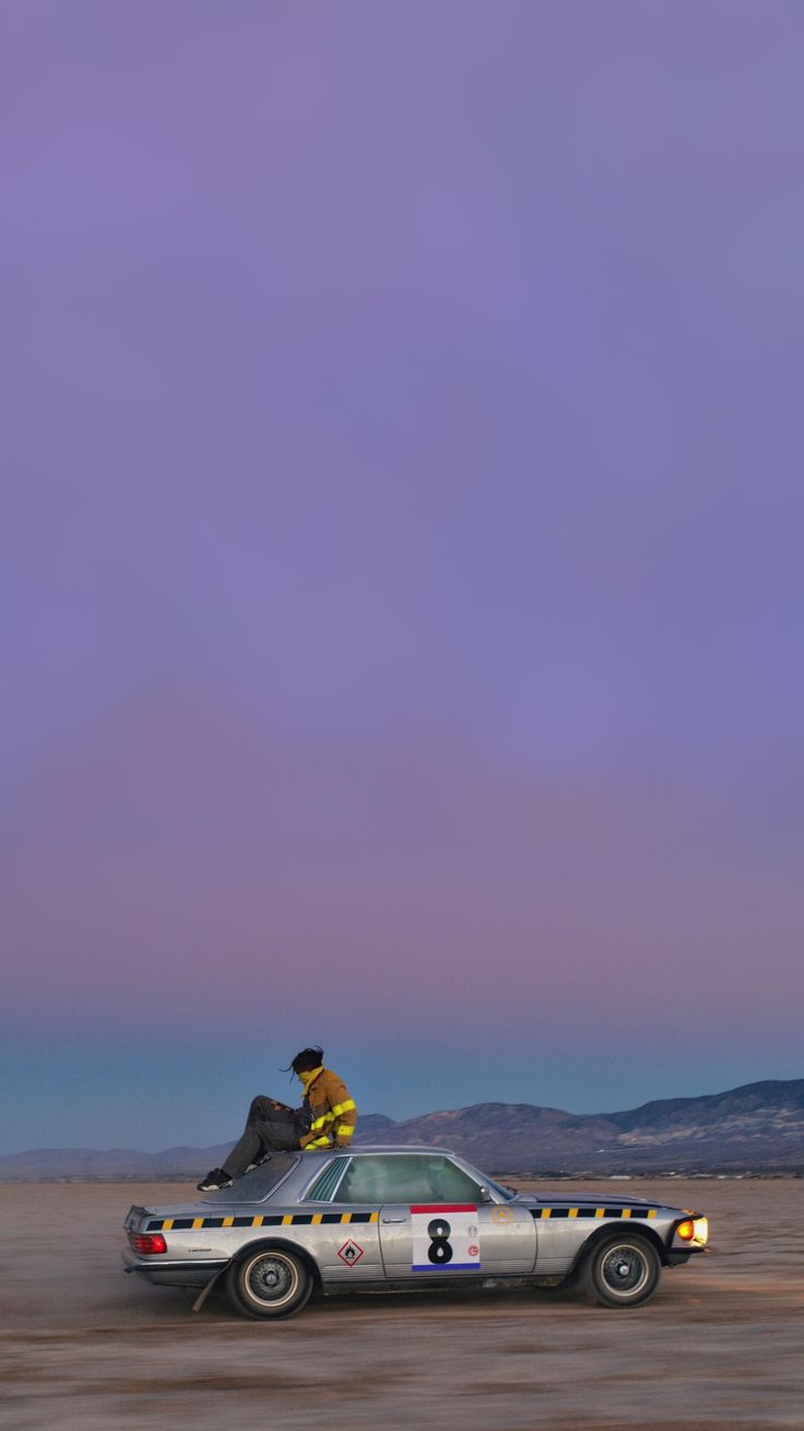 two men sitting on top of a car in the desert