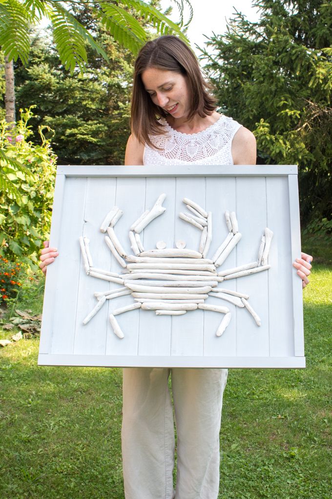 a woman holding up a framed artwork made out of pipes and sticks in the shape of a crab