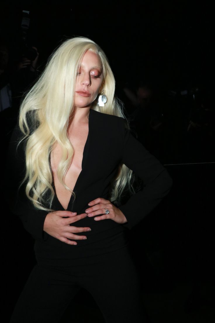 lady with long blonde hair posing for the camera in a black suit and silver earrings