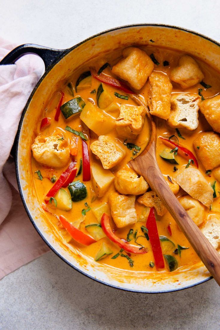 a pan filled with chicken and vegetables on top of a table next to a wooden spoon