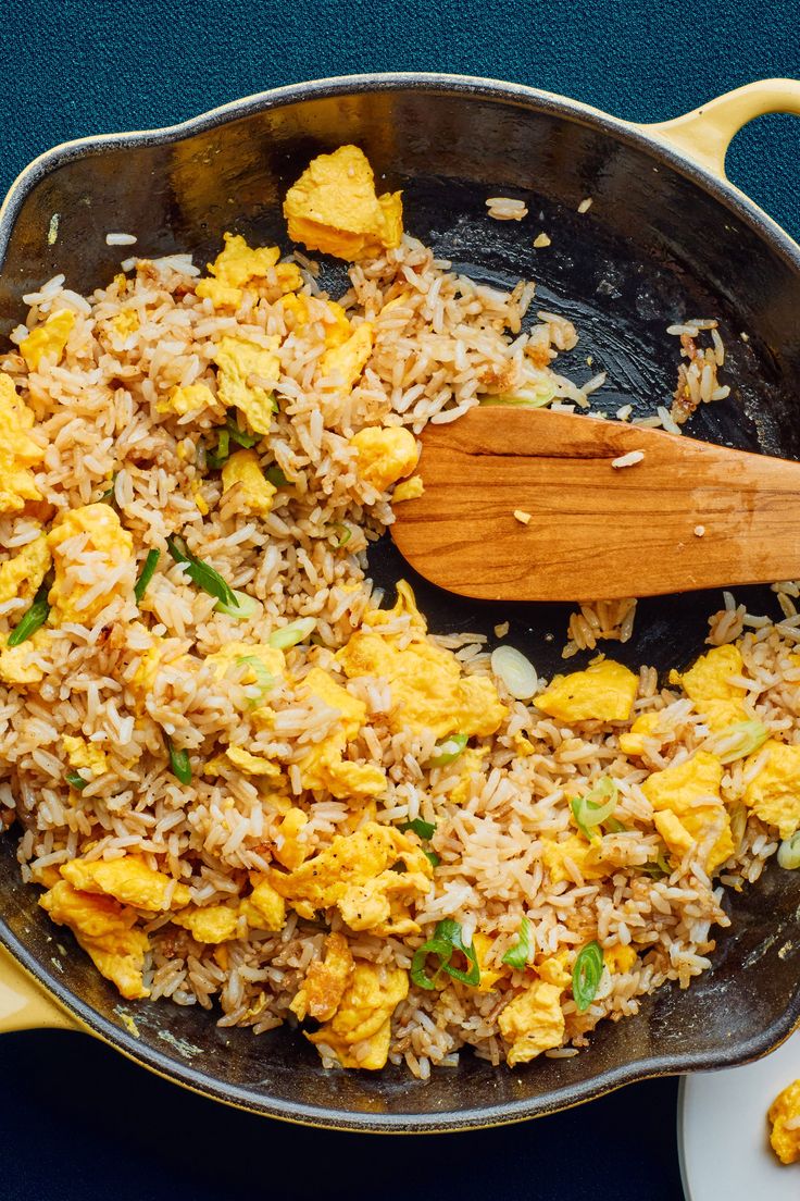 a skillet filled with rice and vegetables on top of a table next to a wooden spoon