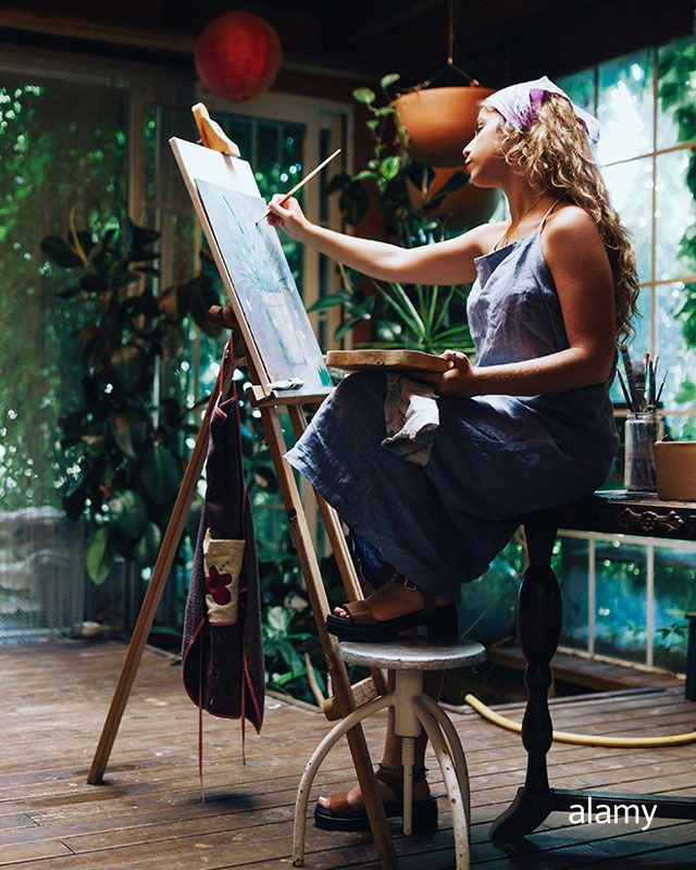 a woman is sitting in front of an easel and painting on the easel