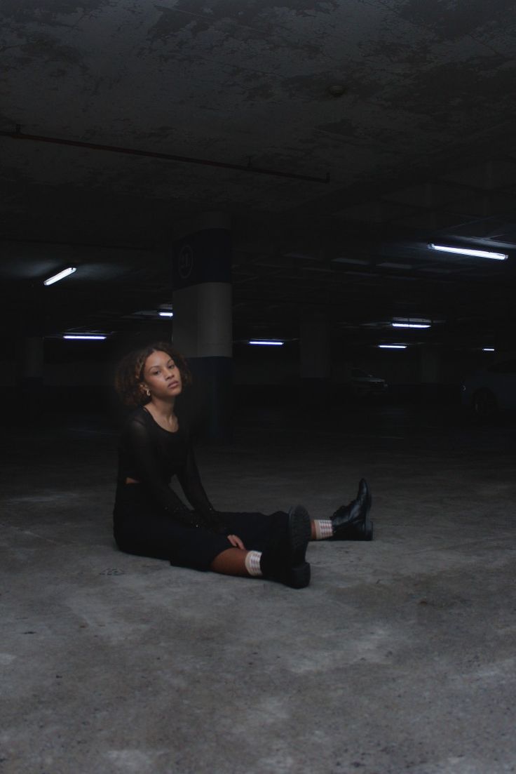 a woman is sitting on the floor in an empty parking garage with her eyes closed