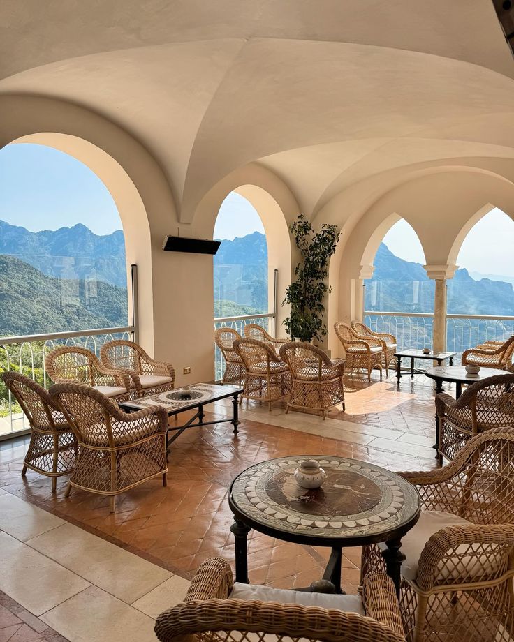 an outdoor seating area with wicker chairs and tables, overlooking mountains in the distance