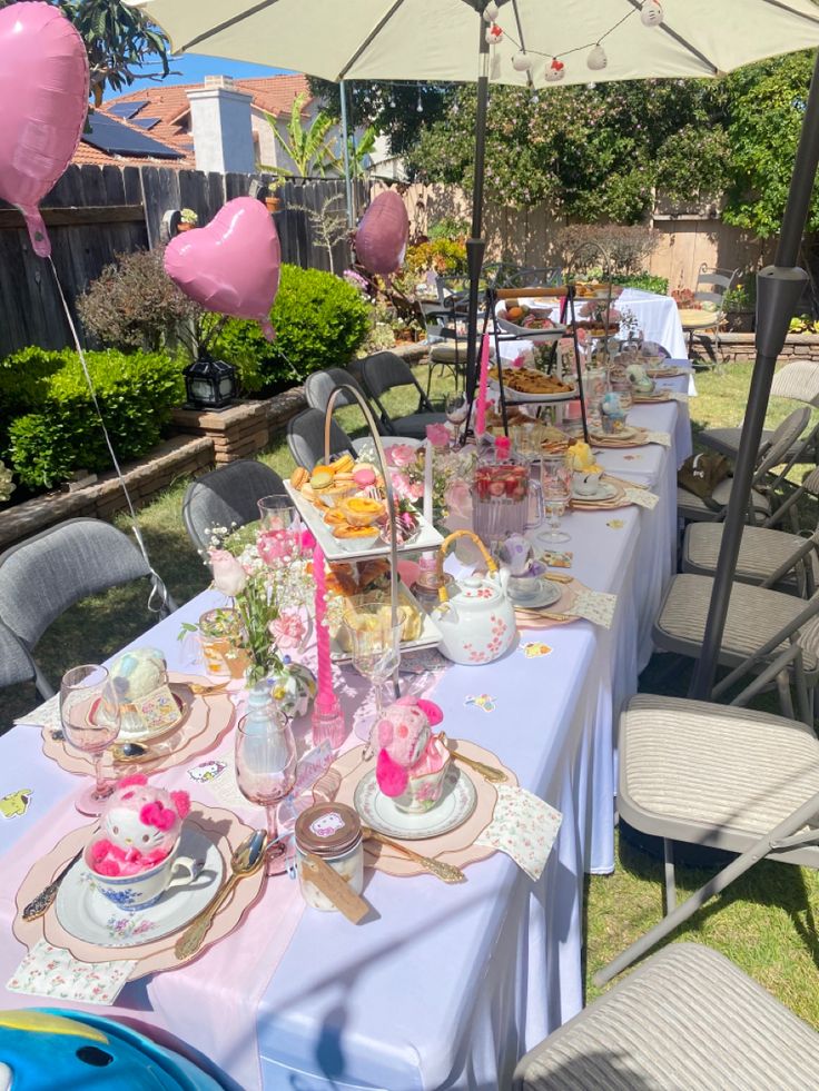 a table set up for a tea party with pink balloons