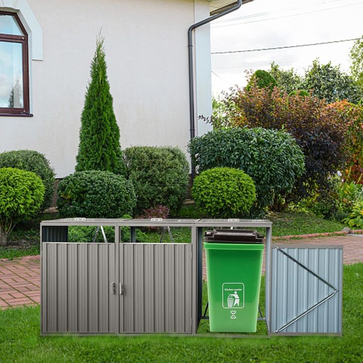 a green trash can sitting next to a metal trash bin in front of a white house