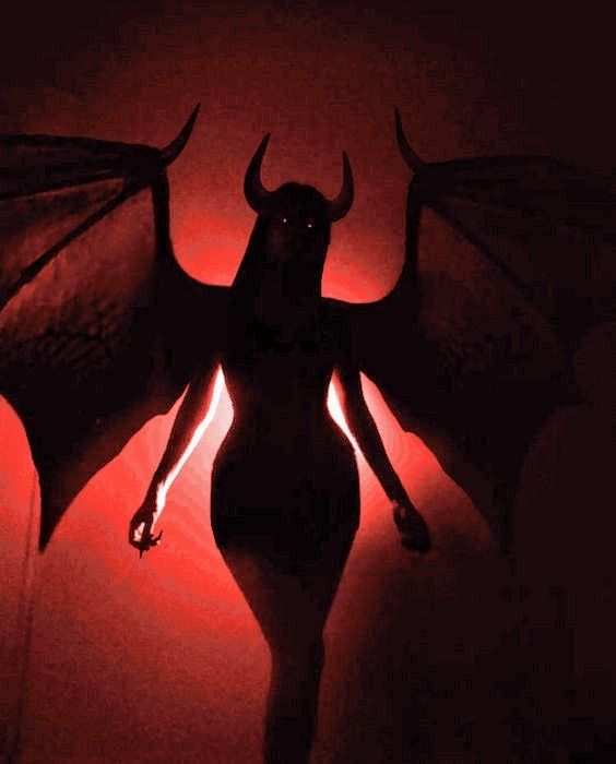 a woman with long hair and horns standing in front of a red light, casting a shadow on her body