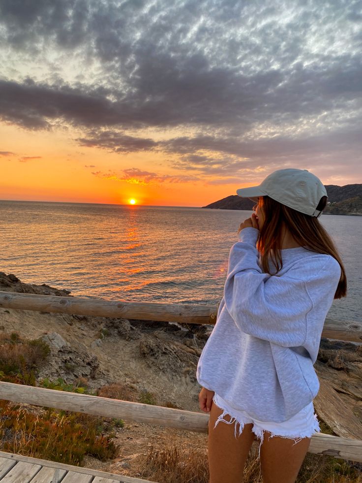 a woman standing on top of a wooden deck next to the ocean at sunset or sunrise