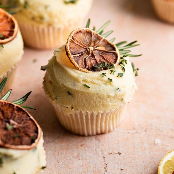 cupcakes with orange slices and herbs on top, sitting next to each other