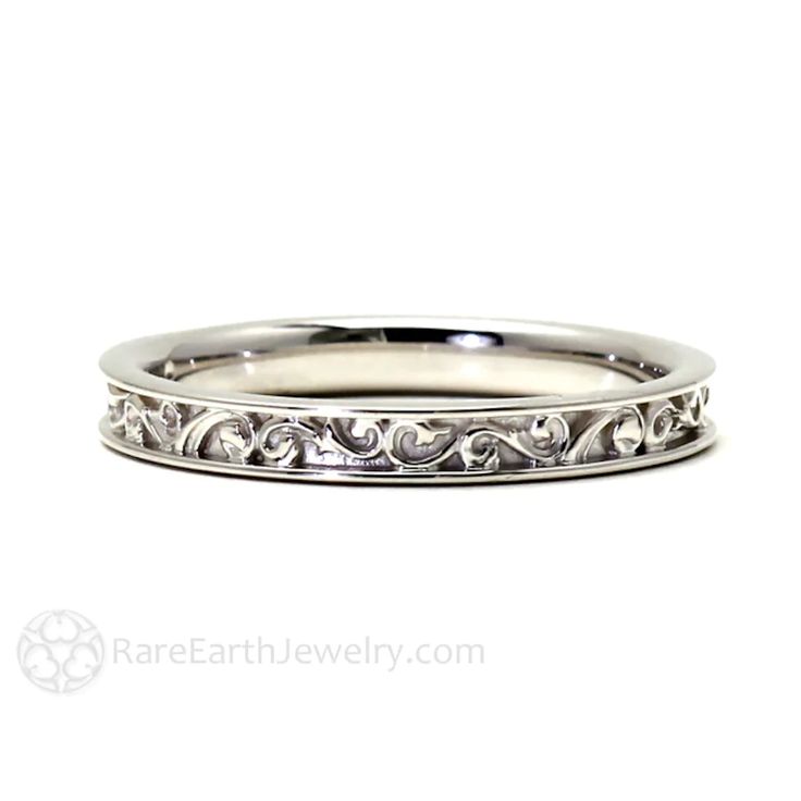 a white gold wedding ring with scrolls on the side and an engraved design in the middle