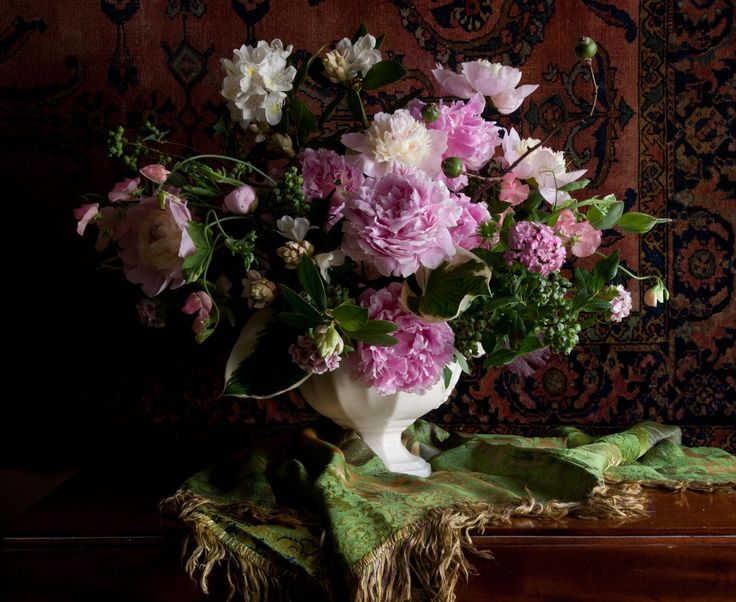 a vase filled with pink and white flowers on top of a wooden table next to a rug