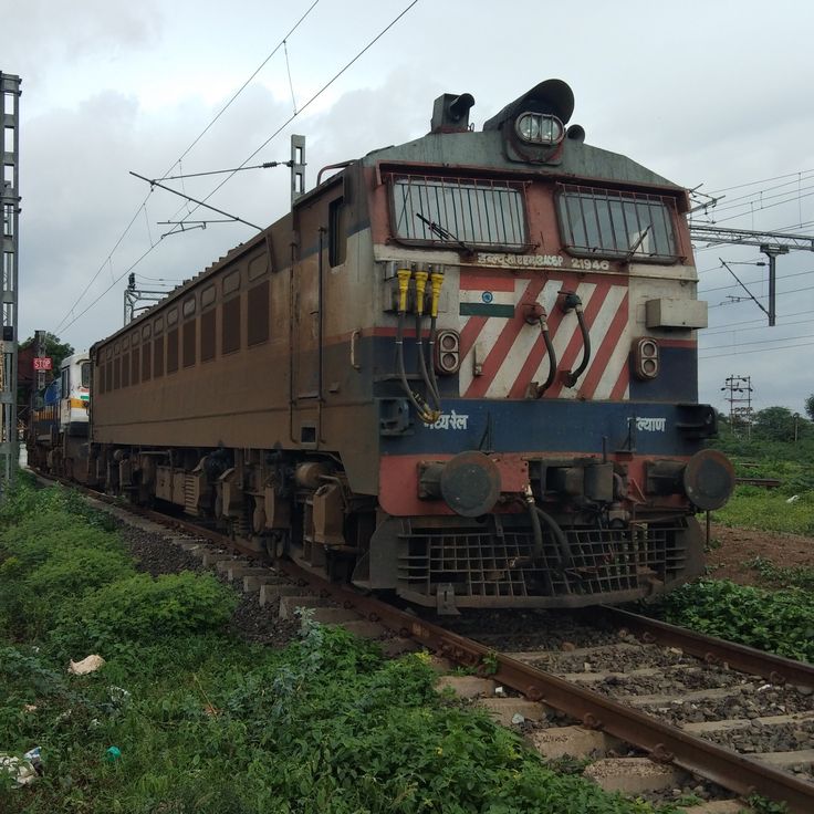 an old train is sitting on the tracks near some weeds and other vegetation in front of it