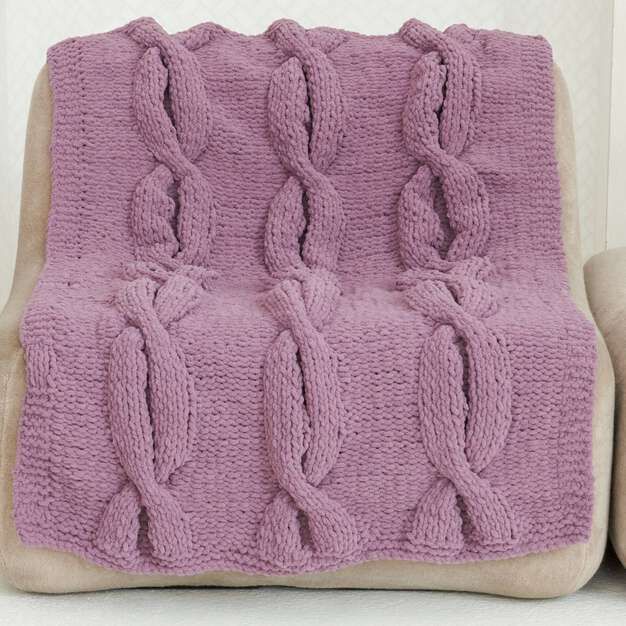 a pink knitted blanket sitting on top of a couch