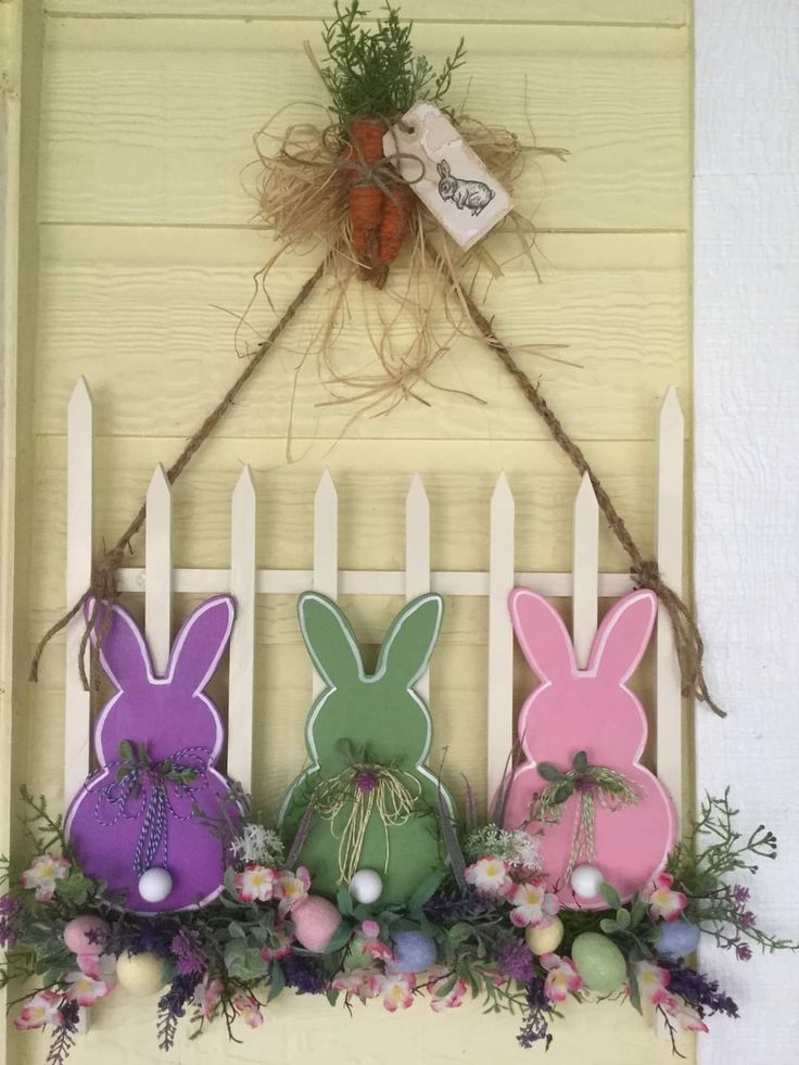 some bunny decorations are hanging on the wall next to a white picket fence with grass and flowers