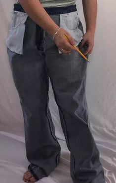 a person standing in front of a white backdrop holding a pencil and wearing grey pants