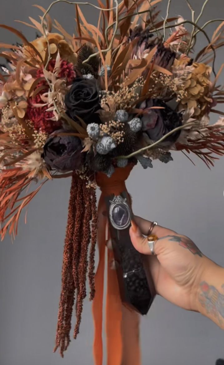 a person is holding a bouquet with flowers and feathers on it, in front of a gray background