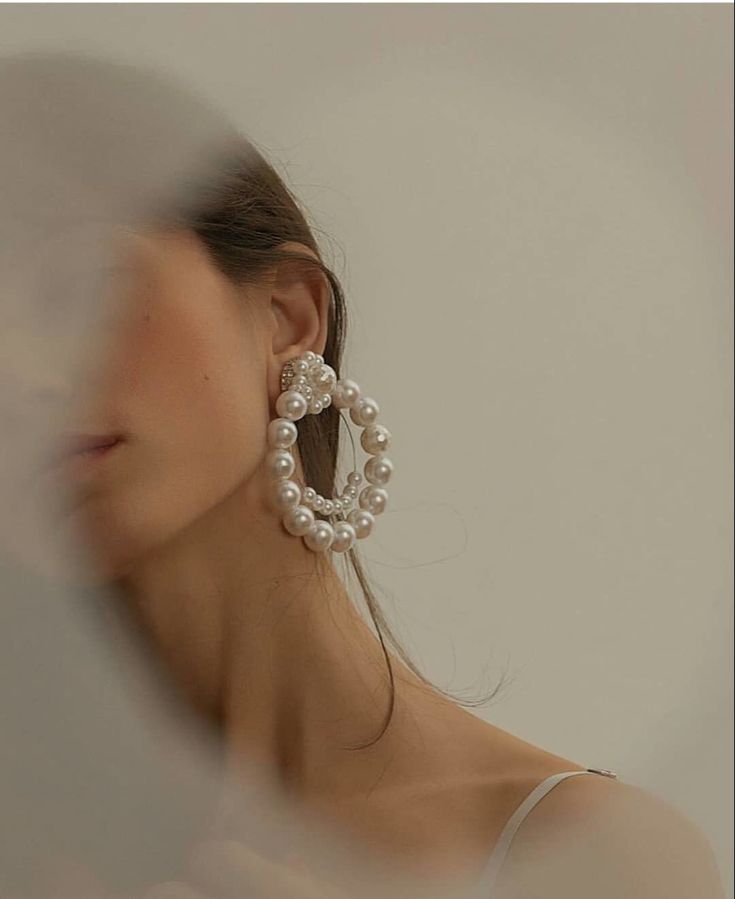 a woman wearing large earrings with pearls on them