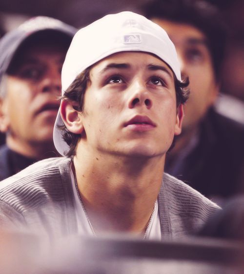 a young man wearing a white hat and sitting in front of other men at a sporting event