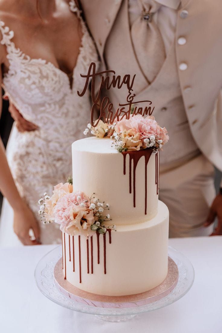 a bride and groom standing next to a wedding cake with chocolate drips on it