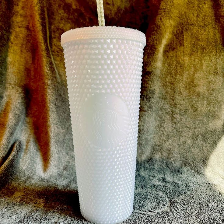 a white cup with a straw in it sitting on a gray surface next to a brown blanket