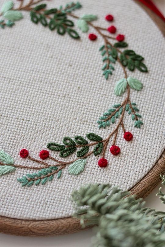 a close up of a embroidery on a piece of cloth with holly and red berries