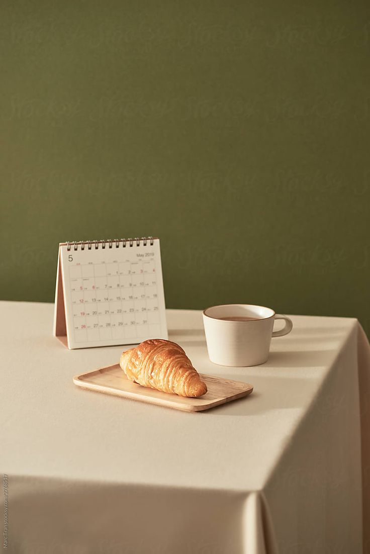 a croissant sitting on top of a table next to a cup and calendar