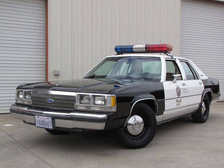 an old police car parked in front of a building with two garage doors on the side