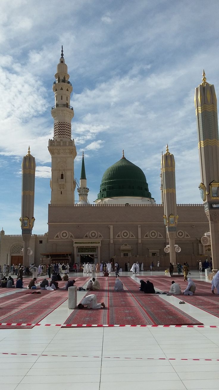 many people are sitting on the ground in front of a large building with a green dome