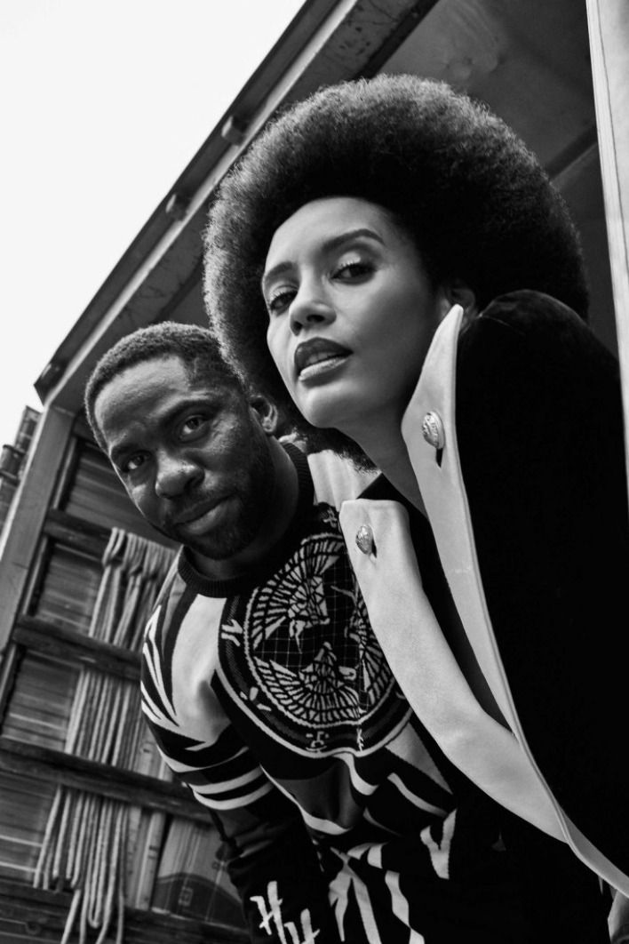 a man and woman standing next to each other in front of a building with an afro hairstyle